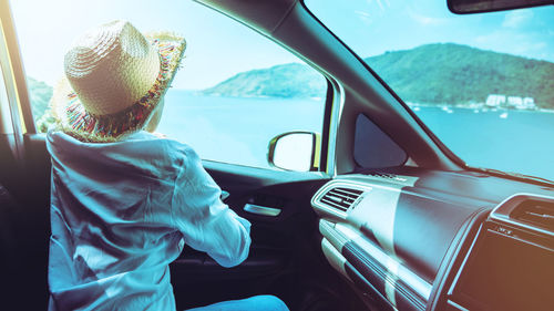 Rear view of woman looking at sea through car window