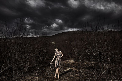 Woman standing on field against dark cloudy sky