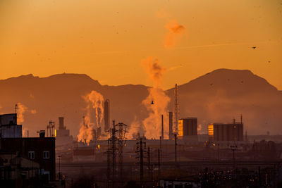 Smoke emitting from factory against sky during sunset