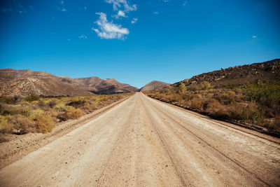 Dirt road leading towards mountains against blue sky