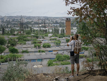 Rear view of man photographing while standing against cityscape