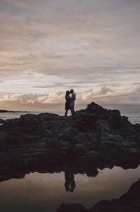 Men standing on rock against sky during sunset