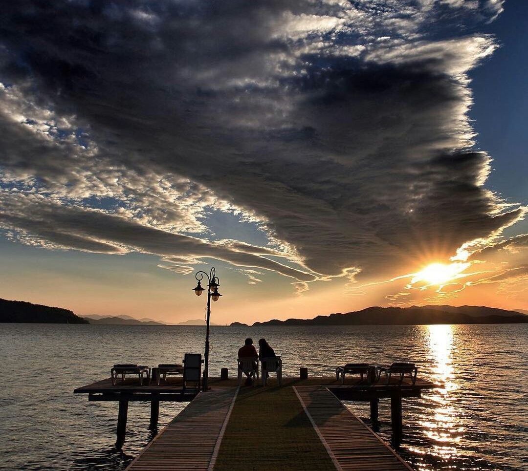 water, sea, pier, tranquility, tranquil scene, sunset, jetty, tourist, dusk, tourism, full length, atmospheric mood, sky, scenics, the way forward, long, cloud, vacations, sitting, men, railing, cloud - sky, distant, sun, calm, idyllic, candid, dramatic sky, hobbies, narrow, ocean