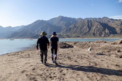 Couple holding hands while walking outdoors with natural landscape of mountains and lake.