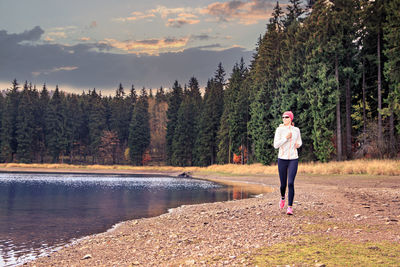 Full length of woman running by lake against sky