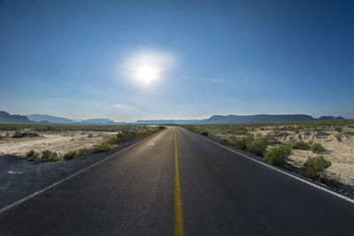 Road amidst field against blue sky