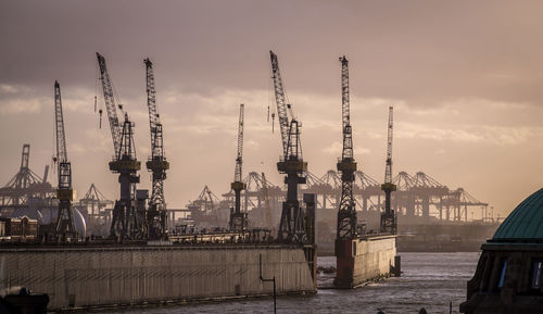 Cranes at commercial dock against sky