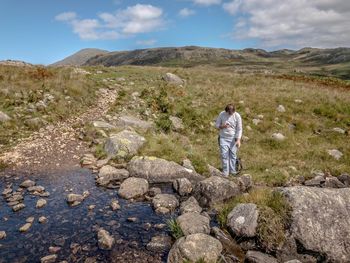 Rear view of man standing on rock against sky