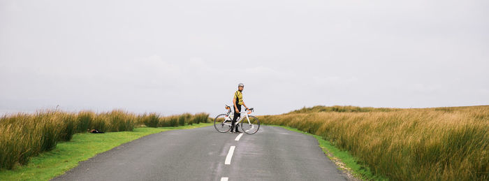 Man riding bicycle on road amidst field against sky