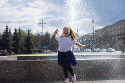 Happy little cute girl having fun in splashes a fountain