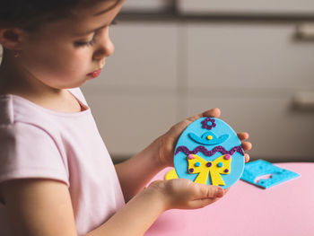 A little caucasian girl is holding a felt sticker easter egg in her hand