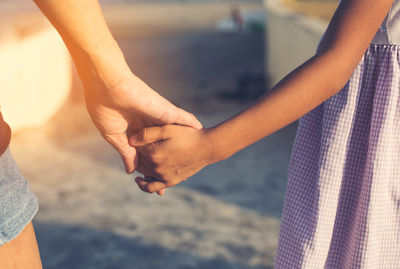 Midsection of mother and daughter with holding hands standing outdoors