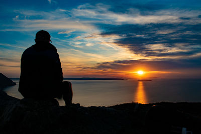 Silhouette man looking at sea against sky during sunset