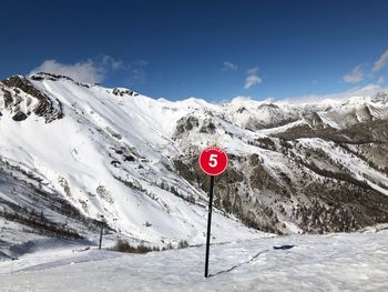 Road sign on snow covered mountain against sky
