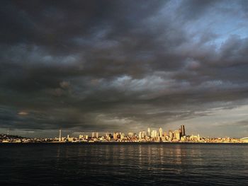 City at waterfront against cloudy sky