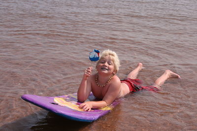 Portrait of teenage boy holding lollipop while lying on inflatable at beach