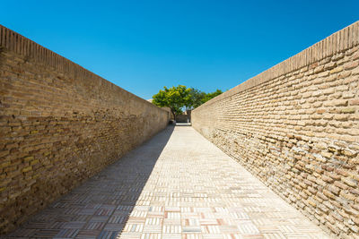 Footpath amidst wall against clear blue sky