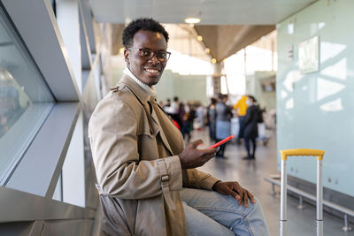 Portrait of young man using mobile phone sitting at airport