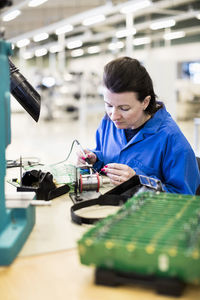 Female technician soldering circuit board at desk in industry
