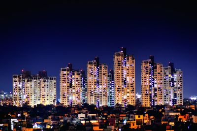 Illuminated cityscape against clear blue sky at night