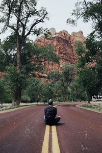 Rear view of man sitting on road against mountain