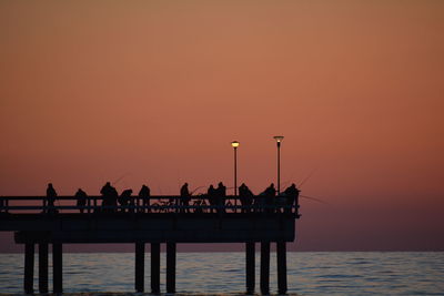 Silhouette people on pier over sea against clear sky during sunset