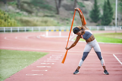 Female athlete stretching resistance band while standing on running track