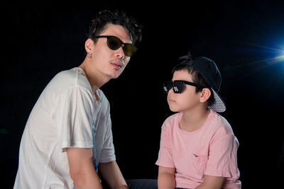 Man and little boy with sunglasses sit looking camera on dark studio background , asian family