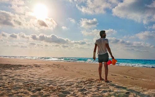 Rear view of woman standing on beach against sky