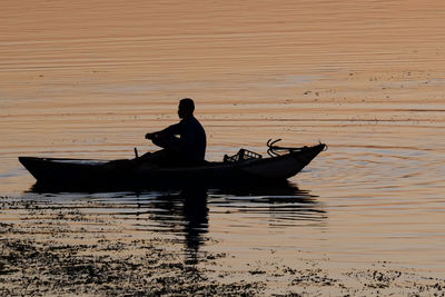 Silhouette man in boat against sea during sunset