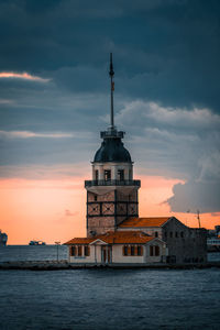 Lighthouse by building against sky during sunset