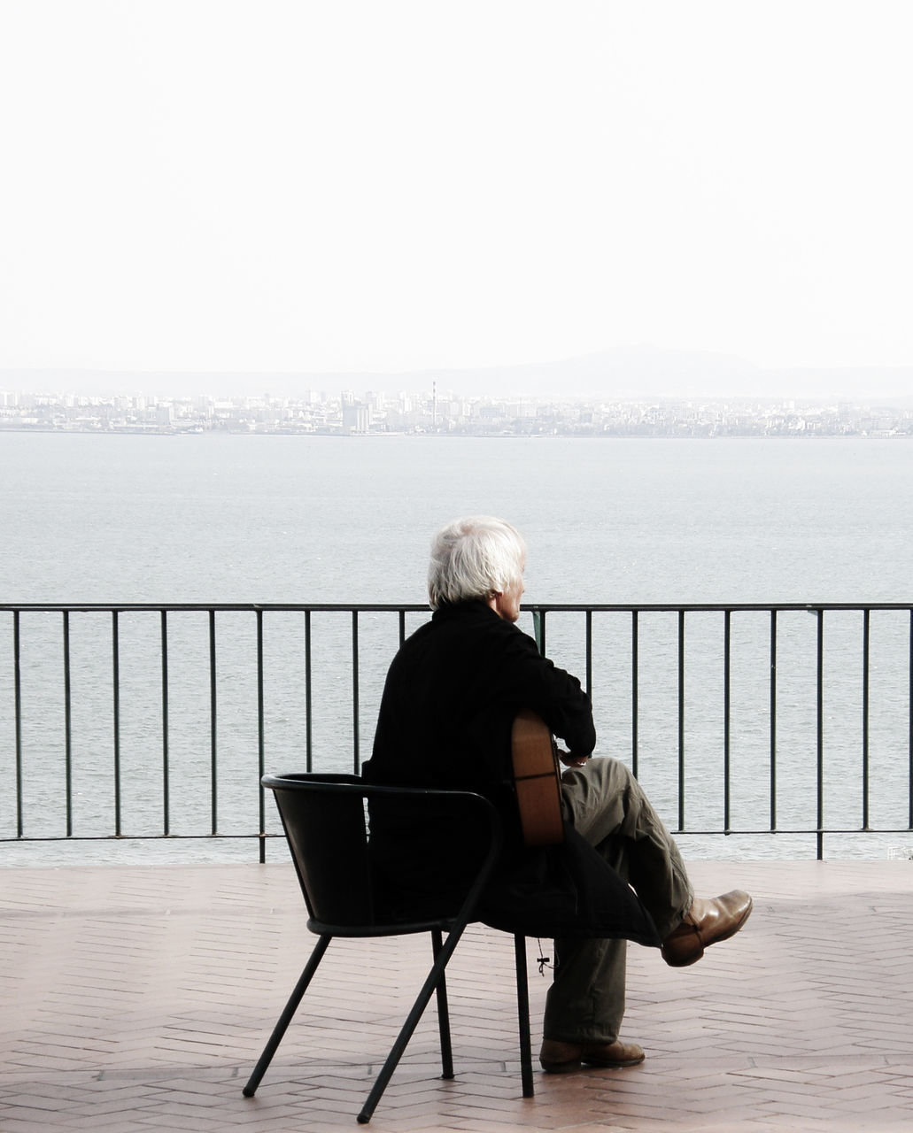 rear view, sitting, water, lifestyles, sea, leisure activity, relaxation, full length, person, bench, looking at view, clear sky, copy space, casual clothing, horizon over water, chair, tranquility, men