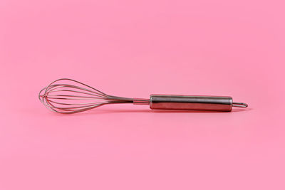 Close-up of wire whisk on pink background