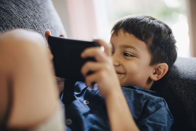 Smiling boy using phone while lying on sofa