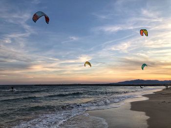 People paragliding on beach against sky during sunset