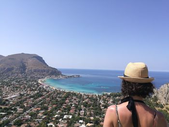 Rear view of woman wearing hat against cityscape by sea