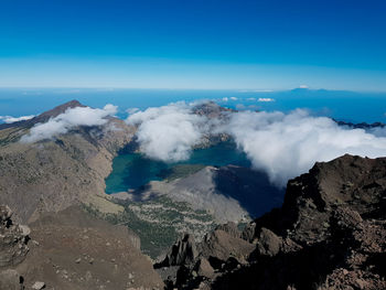 Smoke emitting from volcanic mountain against blue sky