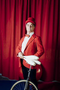 Circus performer holding juggling pins while standing with unicycle in circus