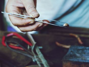 Close-up of craftsperson holding metal with tweezers at workshop