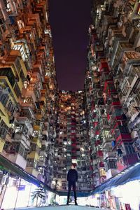 Surface level view of man standing amidst buildings in city at night