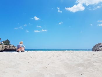 Rear view of overweight woman sitting at beach against sky during summer