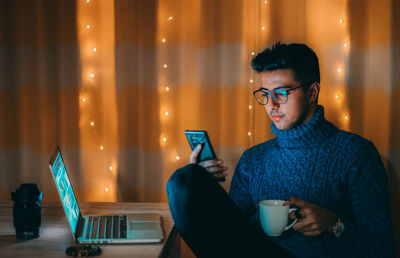 Young man using mobile phone while sitting in laptop