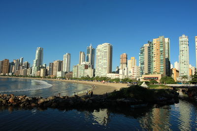 Illuminated city by sea against clear blue sky