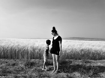 Woman with son standing by wheat field against sky