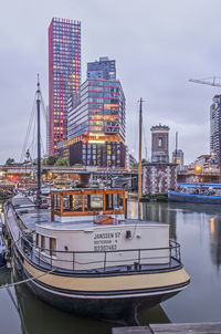 Sailboats moored on river by buildings against sky