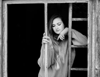 Portrait of young woman standing against window