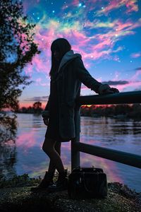 Woman standing at lakeshore against sky during sunset