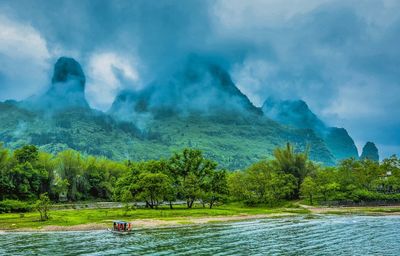 Scenic view of lake by mountains against cloudy sky