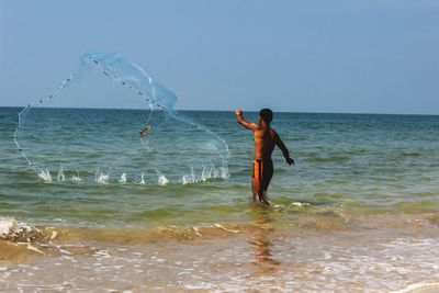 Rear view of shirtless man standing on beach against clear sky