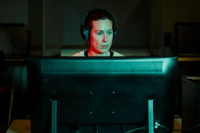 Front view of a woman in headphones working at computer in dark room